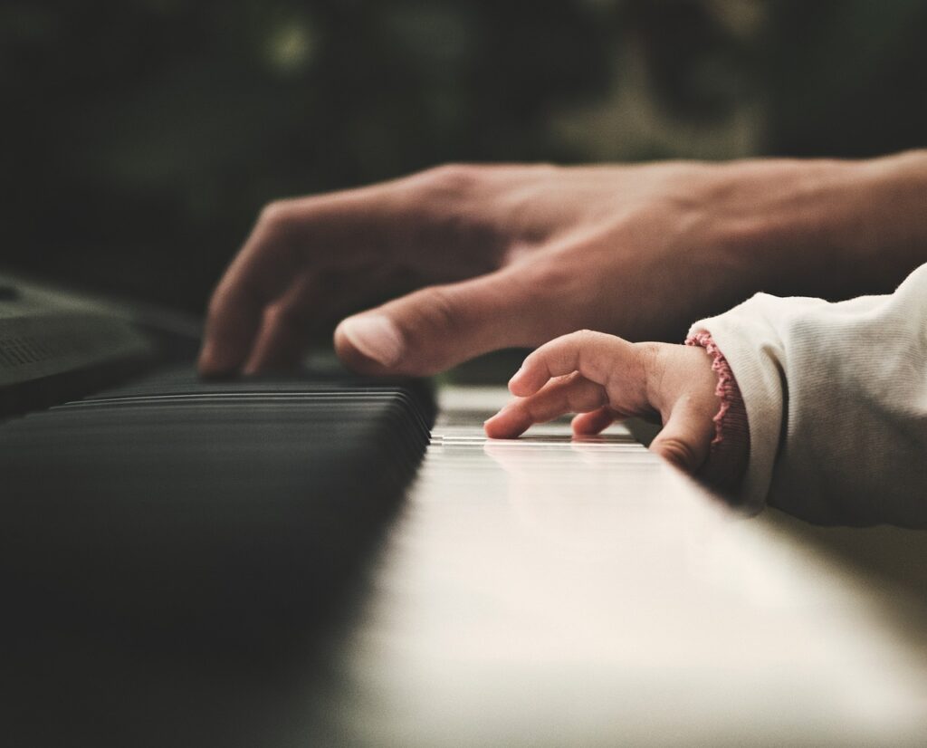 alt="Vue en gros plan des mains d'un adulte et d'un jeune enfant appuyant sur les touches blanches et noires d'un clavier de piano."